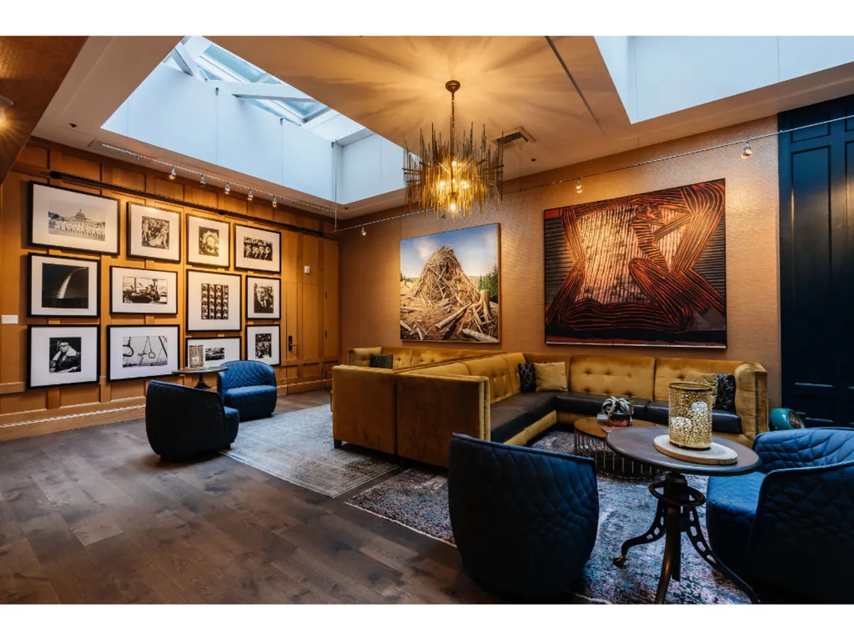A comfortable communal lounge with a chic chandelier, large art pieces adorning the walls, a spacious sectional sofa, and a coffee table, creating an ideal environment for relaxing, socializing, and engaging with curated art.