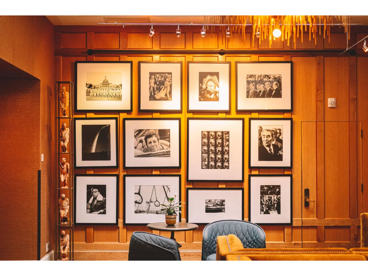 A cozy interior featuring a curated photo wall, a comfortable seating area, and a table with a potted plant. The display of photographs dominates the space, inviting guests to pause and reflect. The overall mood is nostalgic and warm, encouraging art appreciation and connection.