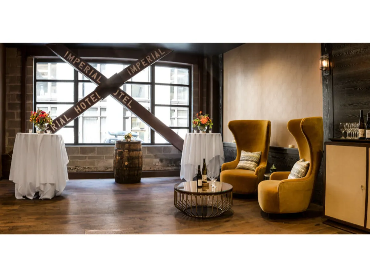 Two yellow armchairs face each other over a small round coffee table, next to two elegantly set tables with white tablecloths and floral arrangements. The setting is intimate and charming, ideal for social gatherings, wine tasting, or celebratory moments.