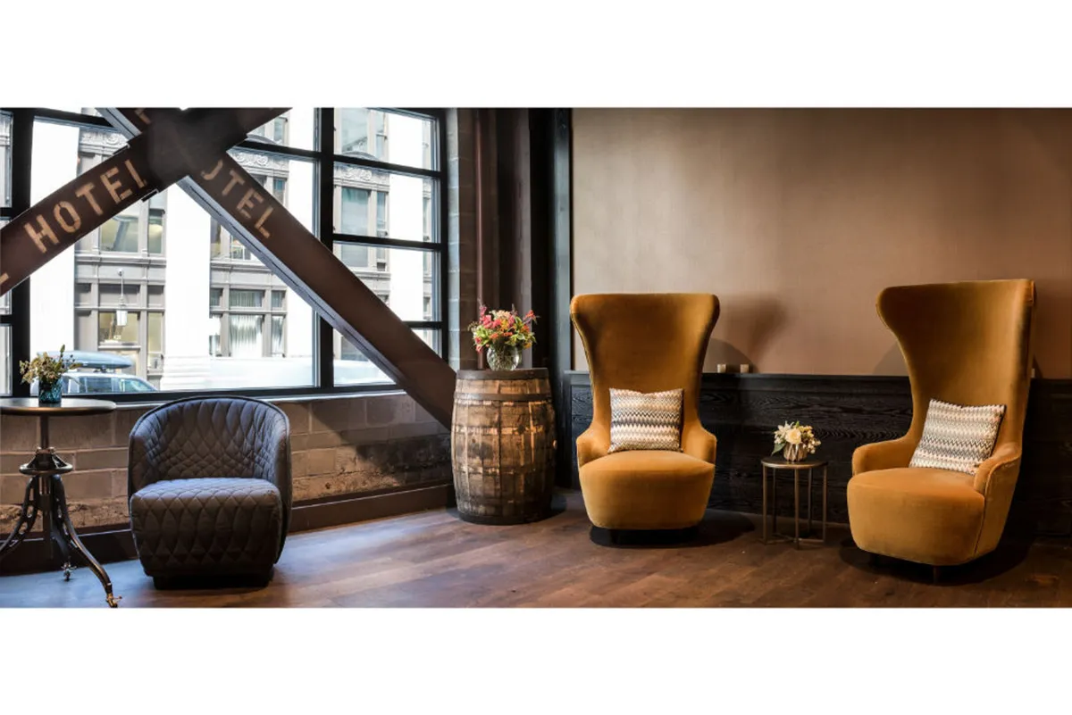This image features two tall, upholstered chairs and a small round table adorned with decorative flowers, creating a cozy, welcoming nook. The barrel-style table and overall arrangement evoke the ambiance of a boutique lounge or cocktail spot, perfect for socializing and unwinding.