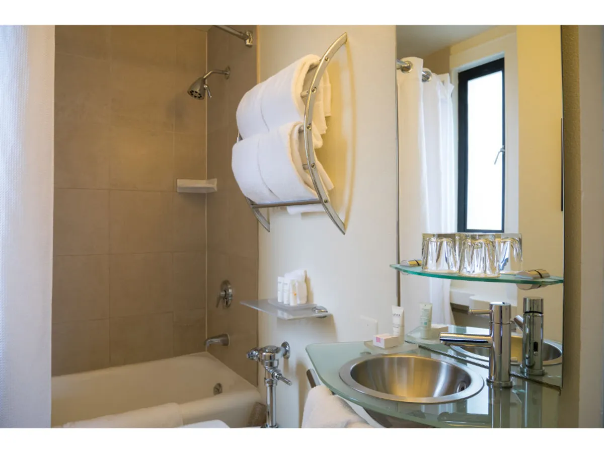 This image showcases a serene and inviting bathroom featuring a bathtub and shower combo, a sleek vanity mirror, neatly folded towels, and a modern sink. The space is bathed in soft light that accentuates the contemporary fixtures, while the overall atmosphere feels relaxing and rejuvenating.