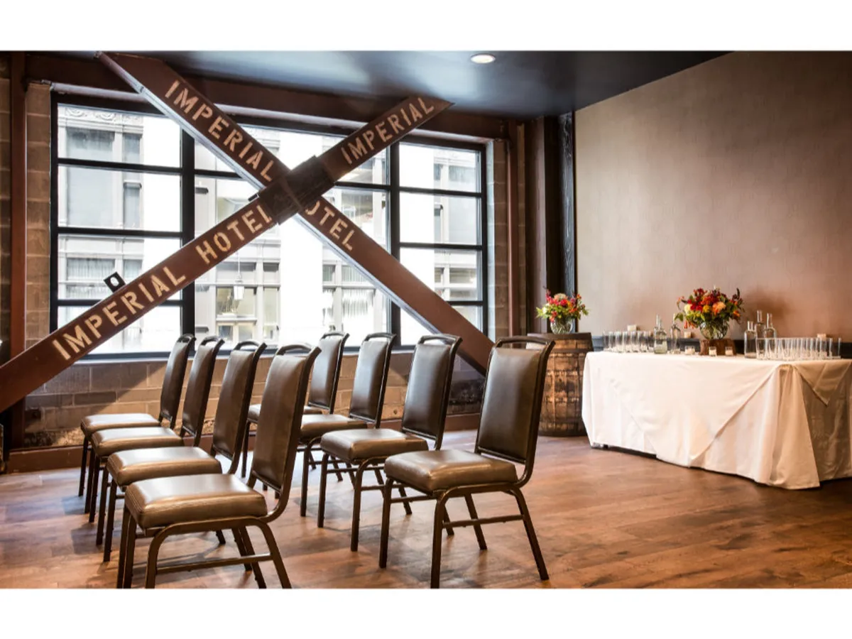 This image shows a stylish meeting space with rows of chairs, a decorated table with flowers, and a large window offering a city view. A decorative beam inscribed with 'IMPERIAL HOTEL' hints at the building's historic roots while the setup suits business meetings or small gatherings.