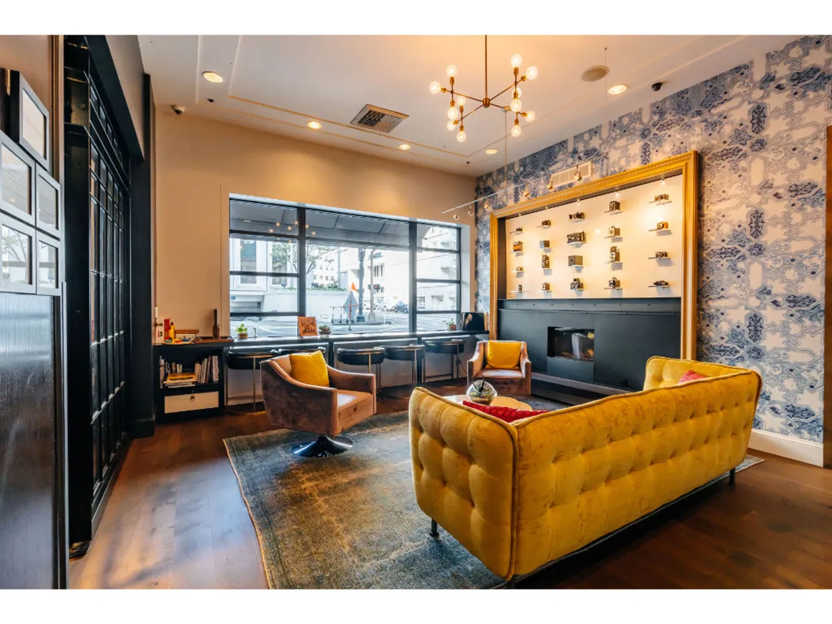 This image features a vibrant lounge setting with a yellow tufted sofa, modern chandelier, two armchairs, and striking blue patterned wallpaper. The decor combines historic charm with contemporary artistic touches, creating an inspiring space ideal for casual meetings, relaxation, or socializing.