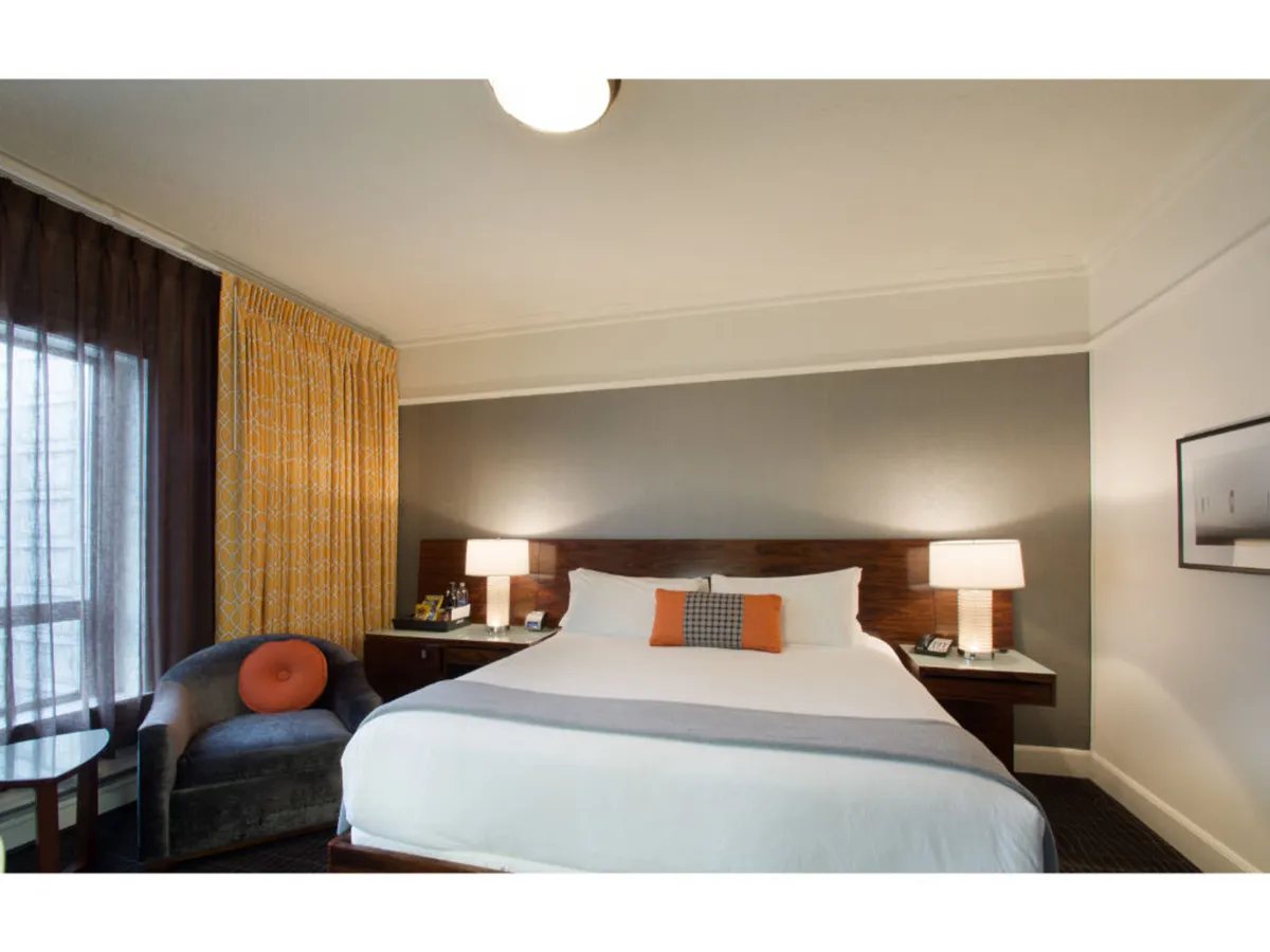 This guest room features a comfortable bed, accent chair, soft lighting, and curtains framing a window—perfect for quiet work sessions, relaxation, or restful sleep.