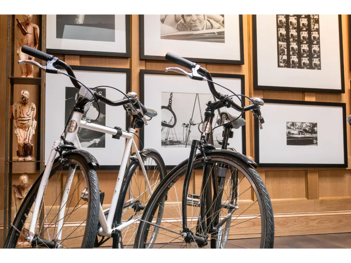 A vibrant interior scene with bicycles and a wall of framed photographs, set against a warm wooden backdrop. The space encourages exploration of local culture, art exhibits, and spontaneous conversations among guests.